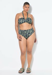 Bikini set met een gedraaide bandeau-top en een hoog geribbelde onderkant in een groen en zwart abstract patroon. Inclusief groene sandaaltjes met accenten.