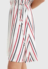 Vit klänning med röda och marinblå diagonala ränder och cirkelmönster, infälld midja och knytbälte för en figurnära silhuett.