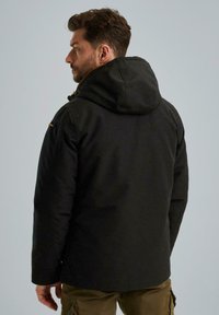 Zwarte hooded jas met een gladde textuur, voorzien van een ritssluiting, een verstelbare capuchon en subtiele schouderaccenten. Zichtbare naden en zakken.