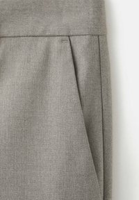 Tissu gris texturé avec un pli vertical et un détail de couture visible, probablement une partie d'un vêtement ou d'un rembourrage.