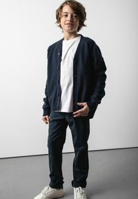 Granatowy kardigan na białej koszulce, w połączeniu z ciemnymi spodniami w kratkę i białymi sneakersami. Zapinany na guziki; miękka faktura materiału.