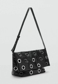Bolso de hombro de cuero negro con ojales circulares de plata, diseño de tapa plegable y correa ajustable. Superficie texturizada con un acabado suave.