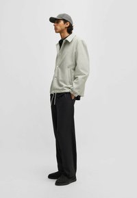 Light gray jacket with button closure, side pockets, and elastic cuffs; paired with black pants and a gray cap. Black sneakers complete the outfit.