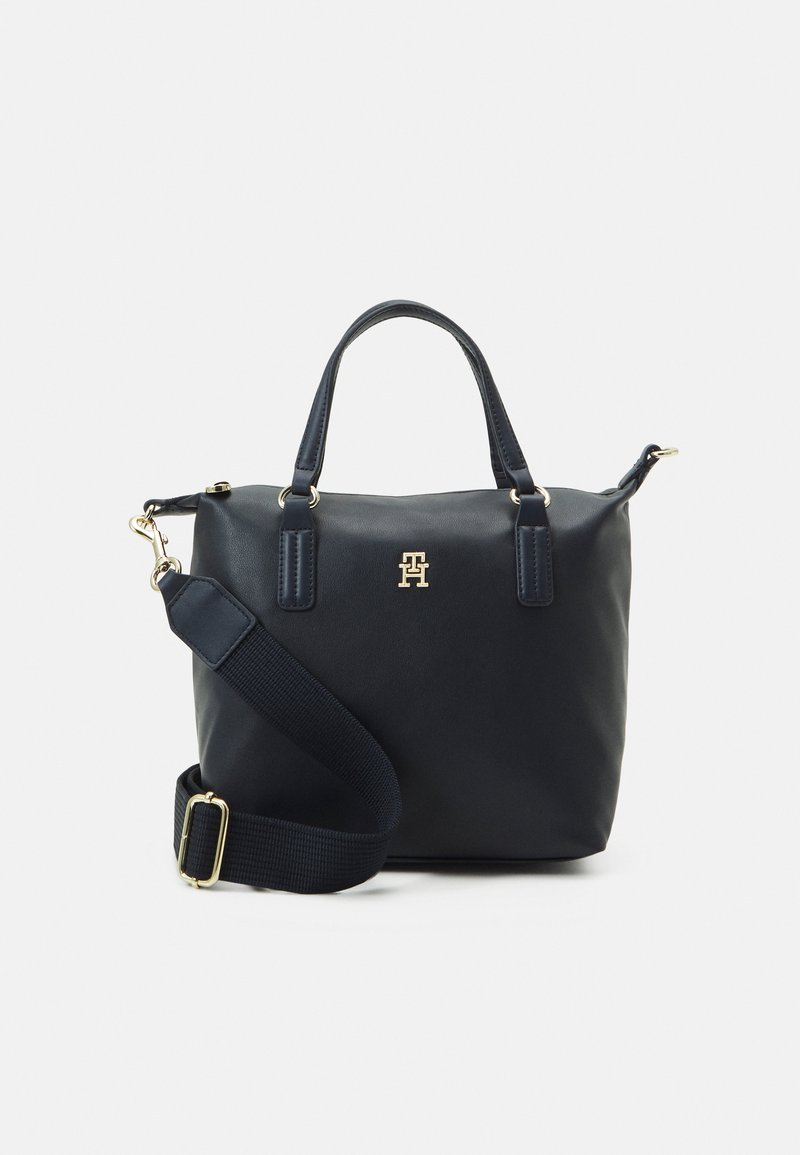 Marineblaue Lederhandtasche mit doppelten Griffen und abnehmbarem Schultergurt, ausgestattet mit vergoldeten Beschlägen und einem auffälligen Logo auf der Vorderseite.