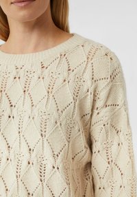 Strickpullover in Creme mit offenem Rautenmuster, mit weitem Ausschnitt und weicher Textur. Eignet sich für schichtweise Stylings.