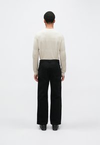 Beežika tooniga tekstuuriga kampsun horisontaalsete triipudega, ühildatud mustade lahtiste pükstega, millel on suured küljetaskud. Mustad kingad lõpetavad komplekti.