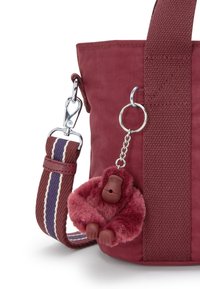 Maroon tygväska med bred randig axelrem och fäst fluffig maroon gorilla nyckelring.