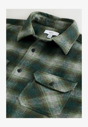 Flanellskjorta i mörkgrön och grå rutigt mönster, med spetsig krage, svarta knappar och en enda bröstficka med lock.