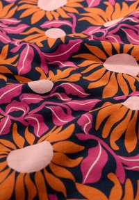 Fabric with a floral pattern featuring large orange flowers, pink leaves, and light pink circles on a dark navy background.