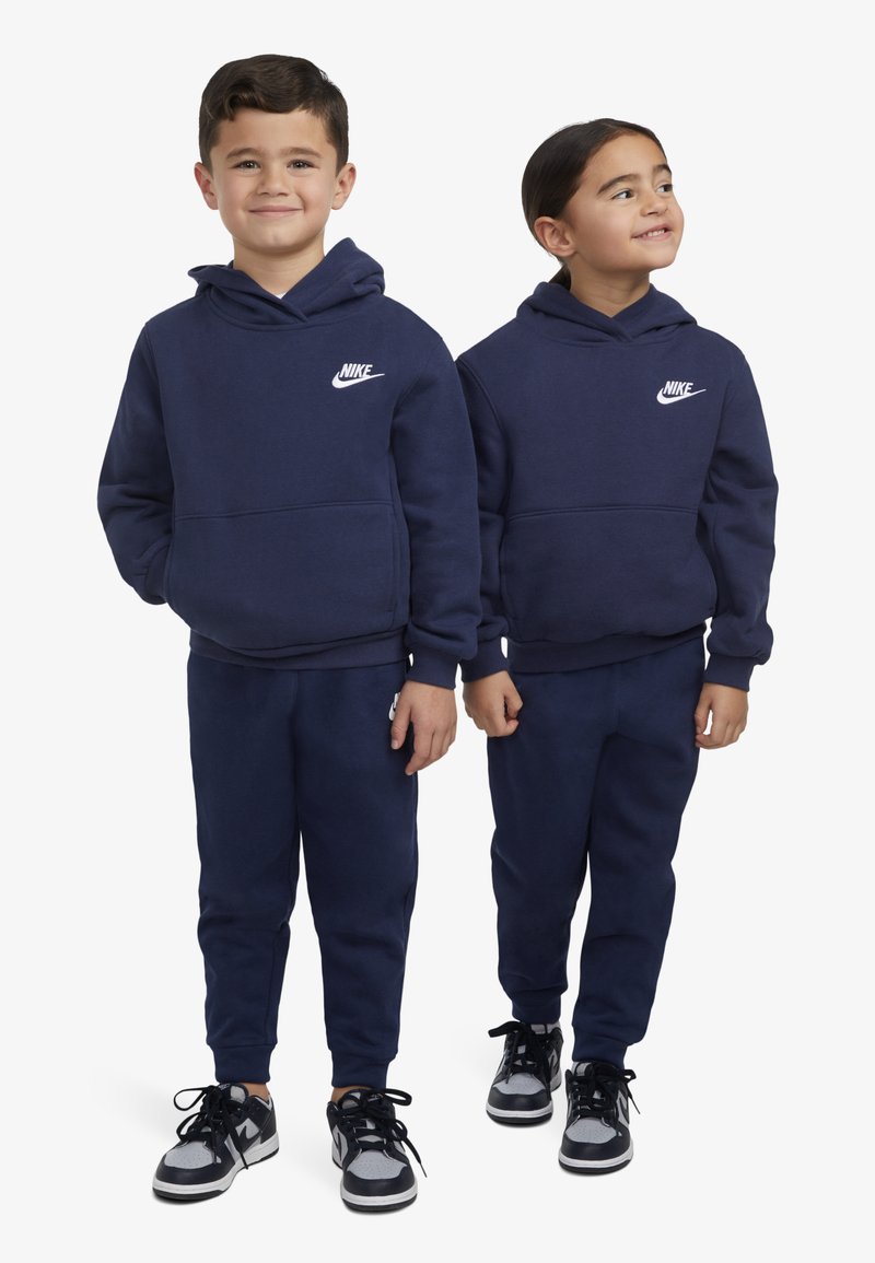 Sweatshirts com capuz azul-marinho, com um bolso frontal e logótipos brancos da Nike, combinados com calças escuras e ténis pretos.