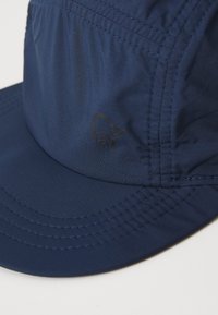 Námornícky modrá čiapka s mierne zakriveným okrajom, vyrobená z ľahkého materiálu. Obsahuje šité detaily a malé čierne logo na boku.