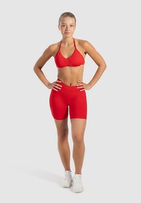 Czerwony biustonosz sportowy z paskami na szyję i marszczeniem, zestawiony z dopasowanymi szortami z wysokim stanem. Gładka, elastyczna tkanina. Białe trampki.