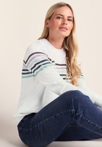 Light gray sweatshirt with horizontal stripes in teal, dark blue, and purple. Sitting pose with dark blue jeans, minimal texture detail.