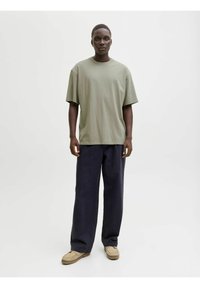 Oliwkowa, oversize'owa koszulka; luźny krój. Połączona z granatowymi spodniami o szerokich nogawkach. Jasnobeżowe buty wsuwane z teksturowaną podeszwą. Minimalistyczny design.