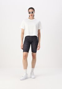 T-shirt blanche raccourcie, shorts de vélo noir à imprimé léopard, baskets blanches et lunettes de soleil. Design simple ; style athlétique décontracté.