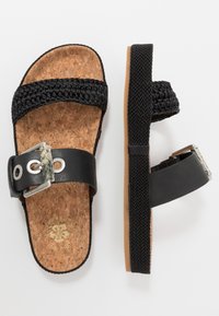 Black cork sandals featuring woven black straps and a matte black buckle with a textured accent. Lightweight cork footbed for comfort.