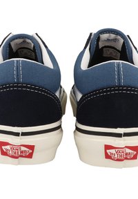 Blue and navy canvas low-top sneakers with white soles, contrasting stitching, and red "VANS Off the Wall" logo on the heel.