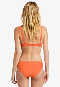 Oranssi urheiluliiveillä varustettu bikinit, joissa on säädettävät hihnat ja takanappi. Designsissä on saumaton istuvuus ja kohtuullinen peittävyys mukavuutta varten.