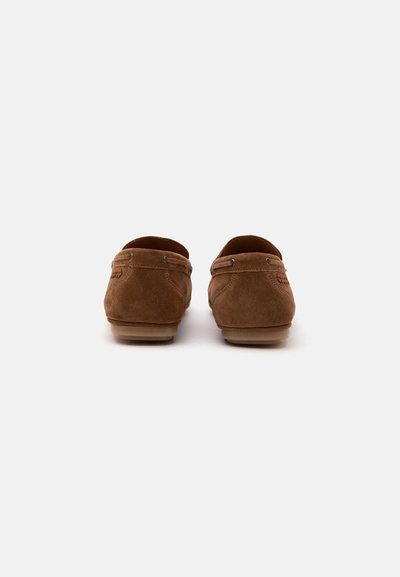 Paire de mocassins en daim marron vue de dos avec coutures visibles et semelles en caoutchouc sur fond blanc.