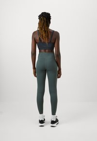 Sötét szürke sportmelltartó állítható pántokkal, amelyet magas derekú sötétzöld leggings-szel párosítottak. Fekete-fehér sportcipők, bokáig érő zoknik.