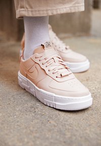 Vaaleanpunaiset nahkaskoot, joissa on valkoinen kumipohja. Kenkien pinnassa on tekstuuri, pyöreä kärki ja nauhakuittaus. Nike-logo sivulla.