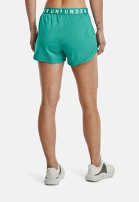 Pantalones cortos deportivos turquesa con una cinturilla elástica blanca que presenta el texto "RUN UNDER". Tejido ligero con un ajuste atlético y diseño con aberturas laterales.