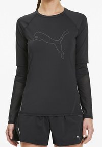 Top sportivo nero a maniche lunghe con tessuto texturizzato e un sottile logo Puma grigio. Abbinato a pantaloni corti neri con piccoli dettagli.