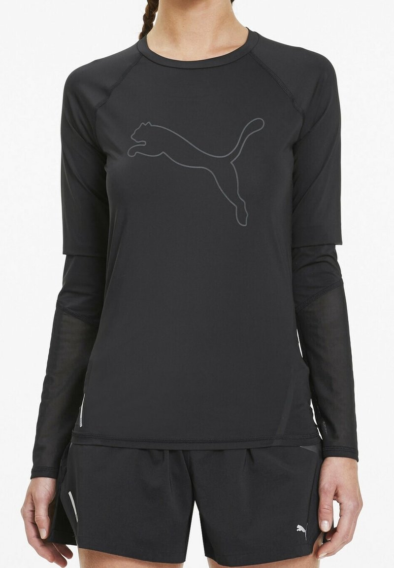 Top sportivo nero a maniche lunghe con tessuto texturizzato e un sottile logo Puma grigio. Abbinato a pantaloni corti neri con piccoli dettagli.