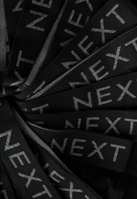 Černé pásky v pase s nápisem "NEXT" stříbrným písmem, vyrobené z elastického materiálu, uspořádané v překrývajících se vrstvách, ukazující hladkou texturu.