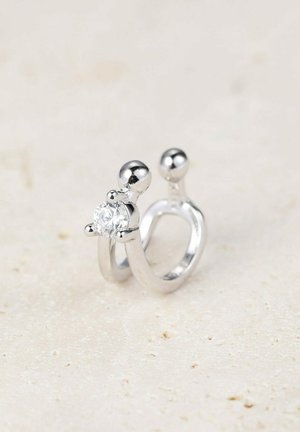 Anello in argento con una pietra centrale trasparente, due sfere arrotondate in cima, texture liscia e un design aperto contemporaneo.