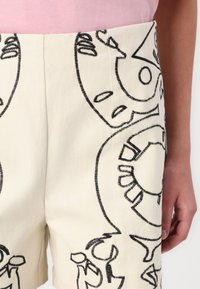 Shorts blancs avec broderies noires présentant des motifs abstraits. Coupe slim, fabriqués dans un tissu résistant avec une texture lisse et un subtil éclat.