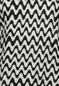 Tessuto in bianco e nero caratterizzato da un motivo a zigzag ondulato. La superficie appare liscia con una leggera lucentezza, indicando un materiale leggero.