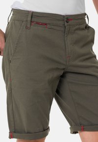Groene katoenen shorts met een ritssluiting, voorzakken en rode accentstiksels. Opgerolde boorden voegen detail toe aan het ontwerp.