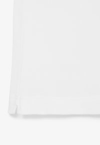 Camisa polo blanca con una tela texturizada, con un dobladillo recto y aberturas laterales. El cuello es de estilo clásico sin logotipos visibles.