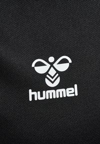 Svart tyg med en texturerad yta som har en vit Hummel-logotyp, kännetecknad av distinkta former och en djärv, modern design.