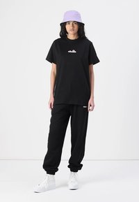 Sort bomulds T-shirt med korte ærmer og et logo, parret med sorte sweatpants. Komplimenteret af en lavendel bucket hat og hvide sneakers.