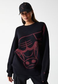 Sort strikkegenser med et stort maroon grafikk av et oksehode på forsiden, rund halslinning og ribbestrikkede mansjetter. Svart caps med logo.