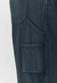 Dark denim cargo pants featuring a large side pocket, angled cut, and textured fabric with visible stitching accents.