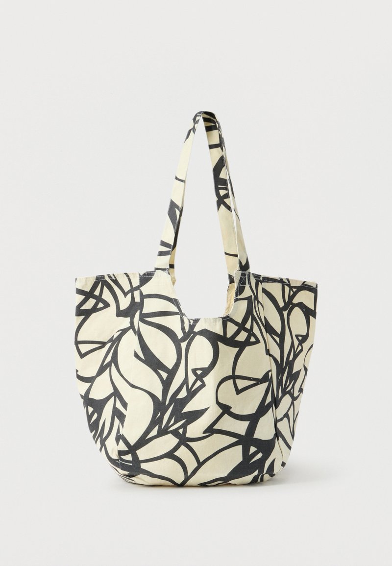 Sac fourre-tout en toile avec un motif abstrait de feuilles noires sur fond crème et des anses longues assorties au motif.