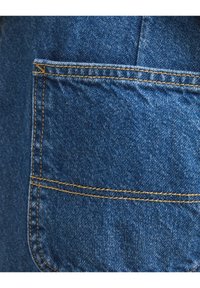 Parche de denim con tela azul de textura tejida distintiva. La costura amarilla de contraste contorna el bolsillo, destacando la artesanía.