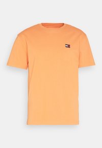 Oranžové bavlněné tričko s krátkými rukávy, kulatým výstřihem a malou nášivkou s logem na levé straně hrudníku. Hladká textura a jednoduchý design.