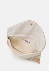 Bolso de tela crema con un diseño decorativo de cuentas y conchas multicolores. Presenta un cierre magnético y un bolsillo interior individual. Etiqueta visible.
