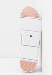 Semelle de basket blanche et rose clair avec grip texturé et logo Tommy Hilfiger au centre de la semelle.