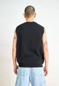Schwarzes ärmelloses Stricktop mit geripptem Saum und Schulteröffnungen, kombiniert mit hellblauen Cargo-Shorts mit Seitentaschen und einer lockeren Passform.