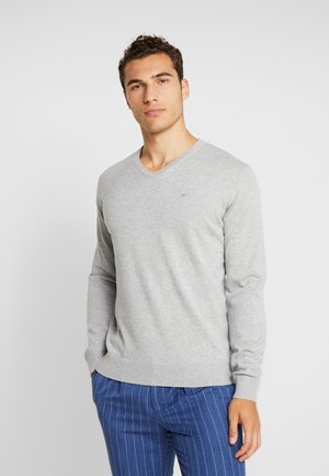 Szary sweter typu V-neck z długimi rękawami, ściągaczami przy rękawach i dołem. Tkanina wydaje się miękka z delikatną teksturą. Małe logo na klatce piersiowej.