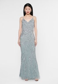 Abito da sera lungo e aderente in blu chiaro con intricate perline argentate e motivi a onde. Presenta spalline sottili e una leggera lucentezza.
