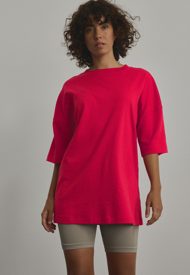 T-shirt rosso oversize con maniche corte, texture a coste e scollatura rotonda, abbinato a pantaloni bike color beige chiaro.