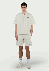 Chemise crème à manches courtes avec un design à boutons, associée à un short assorti avec un motif texturé et un logo noir brodé.
