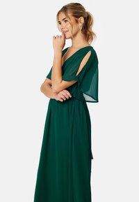 Zelené šaty ke kolenům vyrobené z lehkého materiálu. Mají krátké volánkové rukávy a přiléhavý pas s volnou sukní.