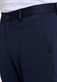 Pantaloni blu navy in tessuto strutturato, con chiusura a bottone, passanti per cintura e tasche laterali, dal taglio slim.